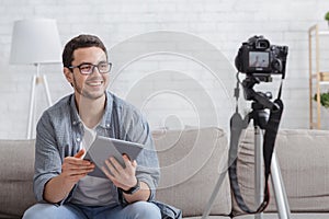 Young attractive man blogger looking at camera and talking on video shooting with devise