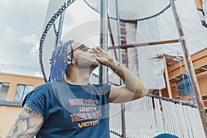 Young attractive man with blue dreadlocks looking at the sun. through sunglasses.