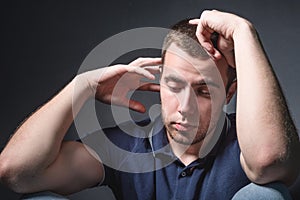 Young attractive man in blue jeans and a polo shirt sits on the floor near the wall in the studio. Youth and