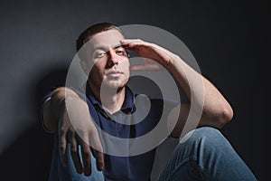 Young attractive man in blue jeans and a polo shirt sits on the floor near the wall in the studio. Youth and