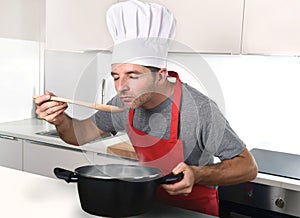 Young attractive man in chef hat and red cook apron testing flavor