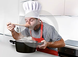 Young attractive man in chef hat and red cook apron testing flavor