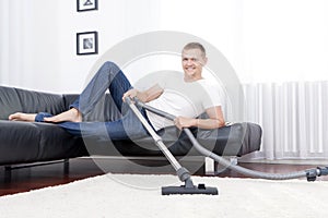 Young attractive man is cleaning vacuum on carpet.