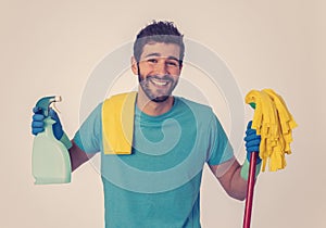 Young attractive man holding cleaning tools and products in bucket isolated in blue background