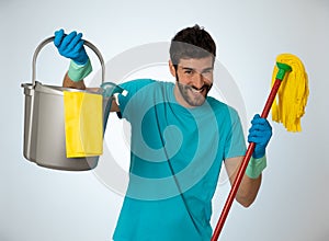 Young attractive man holding cleaning tools and products in bucket isolated in blue background