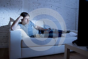 Young attractive man at home lying on couch at living room watching tv holding remote control