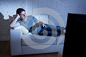 Young attractive man at home lying on couch at living room watching tv holding remote control