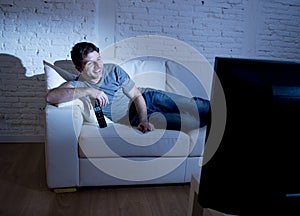 Young attractive man at home lying on couch at living room watching tv holding remote control