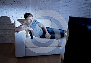 Young attractive man at home lying on couch at living room watching tv holding remote control