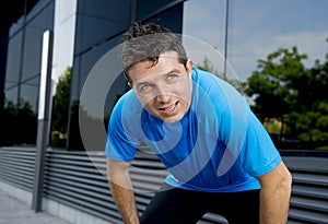 Young attractive man leaning exhausted after running session sweating taking a break to recover in urban street photo