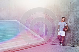 Young attractive man leaning on wall while holding ball