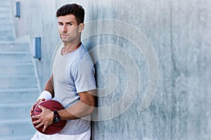 Young attractive man leaning on wall while holding ball