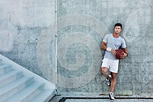 Young attractive man leaning on wall while holding ball