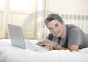 Young attractive man lying on bed or couch enjoying social networking using computer laptop at home