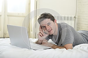 Young attractive man lying on bed or couch enjoying social networking using computer laptop at home