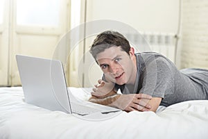 Young attractive man lying on bed or couch enjoying social networking using computer laptop at home