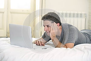 Young attractive man lying on bed or couch enjoying social networking using computer laptop at home