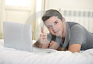 Young attractive man lying on bed or couch enjoying social networking using computer laptop at home