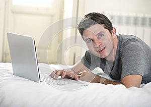 Young attractive man lying on bed or couch enjoying social networking using computer laptop at home