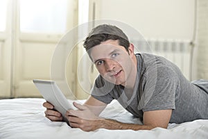 Young attractive man lying on bed or couch enjoying social networking using digital tablet computer internet at home