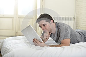 Young attractive man lying on bed or couch enjoying social networking using digital tablet computer internet at home