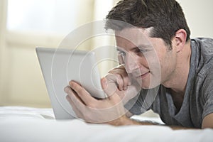 Young attractive man lying on bed or couch enjoying social networking using digital tablet computer internet at home