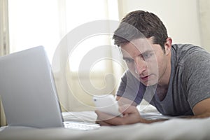 Young attractive man lying on bed or couch using mobile phone and computer laptop internet addict