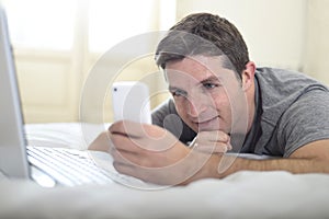 Young attractive man lying on bed or couch using mobile phone and computer laptop internet addict