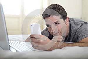 Young attractive man lying on bed or couch using mobile phone and computer laptop internet addict