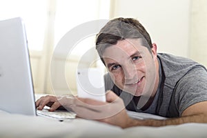 Young attractive man lying on bed or couch using mobile phone and computer laptop internet addict