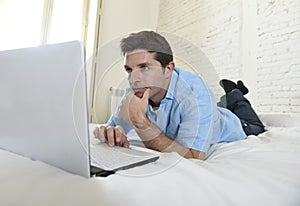 Young attractive man lying on bed enjoying social networking using computer at home