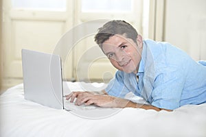 Young attractive man lying on bed enjoying social networking using computer at home