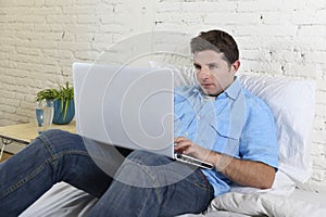 Young attractive man lying on bed enjoying social networking using computer laptop at home
