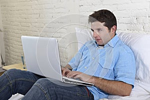 Young attractive man lying on bed enjoying social networking using computer laptop at home