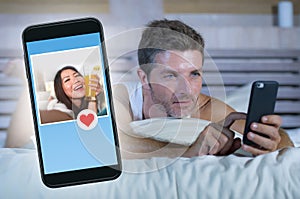 Young attractive man lying in bed on line searching for sex or love finding a beautiful girl profile sending like using mobile pho