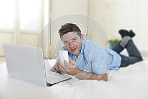 Young attractive man lying on bed using mobile phone and computer laptop working from home