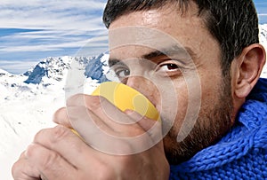 Young attractive man outdoors drinking cup of coffee or tea in cold winter snow mountain