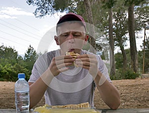 Young attractive man on a picnic eating shawarma sitting at a wooden table, eating in nature, fast food