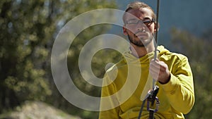 Young attractive man rock climber in the mountains belaying climbing partner and setting up rope, healthy lifestyle and