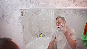 Young attractive man shaving while standing in the bathroom in front of the mirror, back view