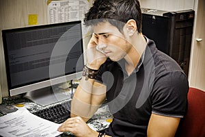 Young Attractive Man Sitting at Computer Desk Talking on Cell Phone