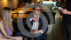 Young attractive man sitting in restauranttogether with his friends and paying bill by credit card. Lifestyle and