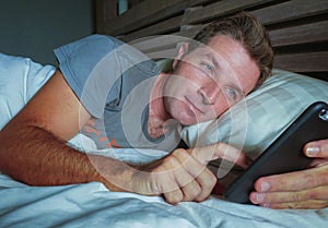 Young attractive man smiling happy lying on bed at night using social media app on mobile phone texting or having video call in co