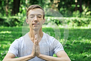 Attractive man in sport clothes is meditating cupped in a meditation or prayer gesture  with a pacified face in the park photo