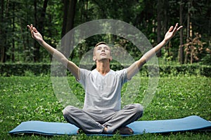 Young attractive man in sport clothes is meditating in the lotus position with a pacified face in the park against the background