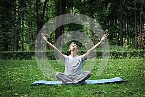 Young attractive man in sport clothes is meditating in the lotus position with a pacified face in the park against the background photo