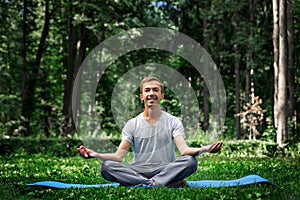 Young attractive man in sport clothes is meditating in the lotus position with a pacified face in the park photo