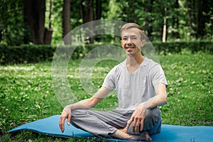 Young attractive man in sport clothes is meditating in the lotus position with a pacified face in the park photo