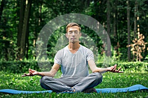 Young attractive man in sport clothes is meditating in the lotus position with a pacified face in the park photo