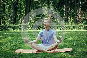 Young attractive man in sport clothes is meditating in the lotus position with a pacified face in the park photo